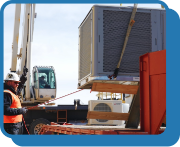 a wide angle of a crane lowering an hvac unit onto the roof of a commercial building