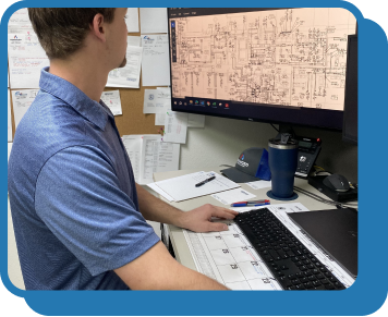 a man in a blue polo sits at a computer desk and looks at a screen